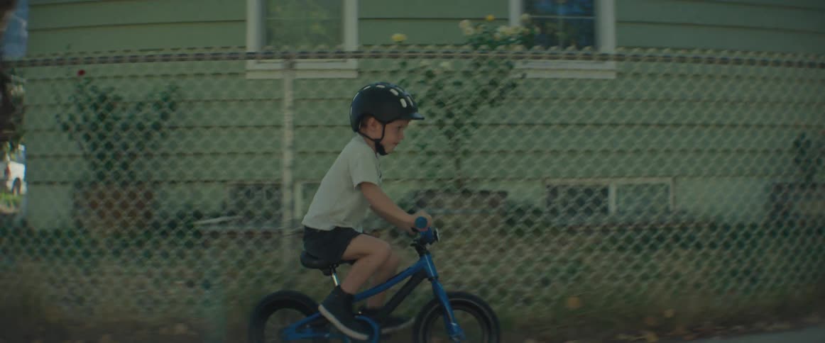 Little boy wearing a helmet riding a bike on the sidewalk in a residential neighborhood