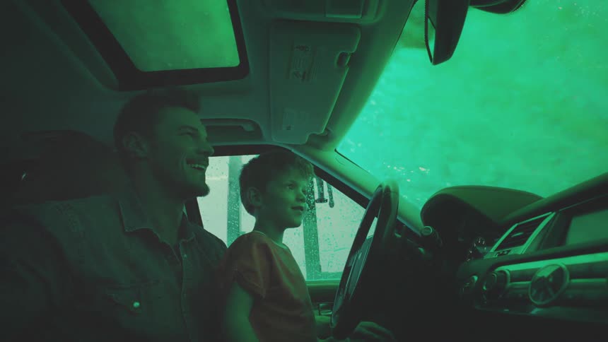 Man with his son sitting in the car seat having fun while the vehicle is being washed in a machine