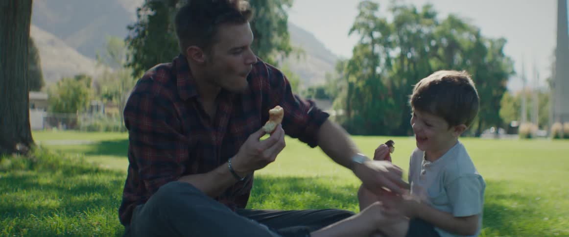 Father sitting on the grass playing with his son and eating a treat
