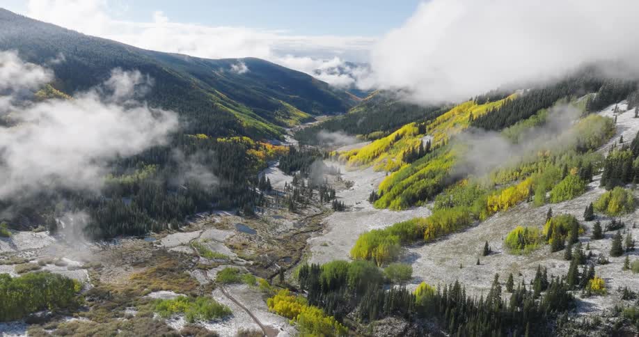 Stream winds through a narrow valley between forest covered mountains in winter