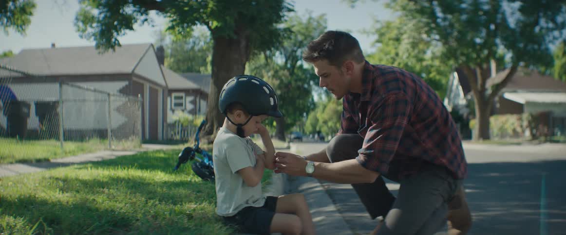 A father applies an adhesive bandage to his sons elbow after the boy fell off his bicycle in the neighborhood