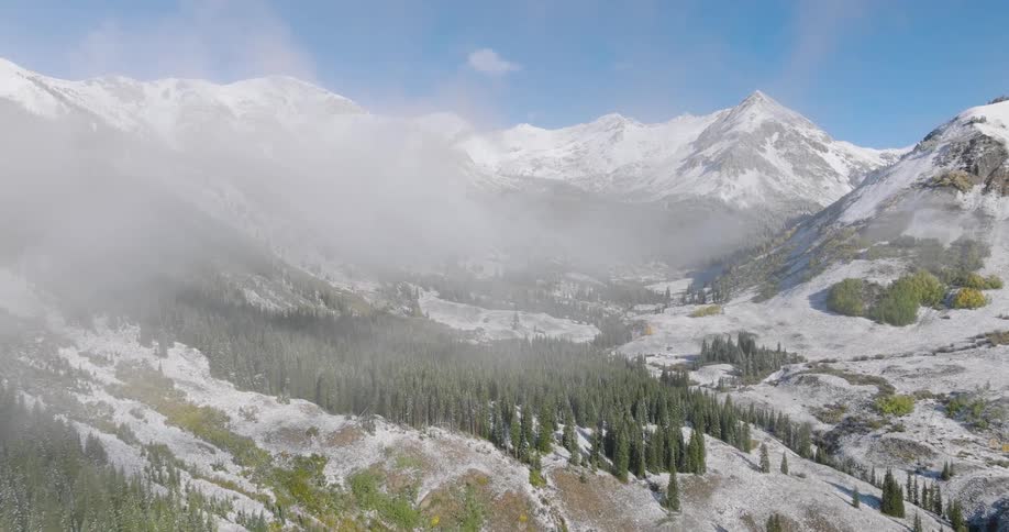 Aerial view of a mountainous landscape with snowcapped peaks a valley covered in a mix of snow and autumn foliage and a river winding through the scene