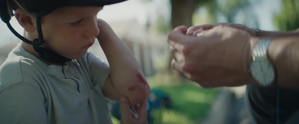Adult hand placing a bandage on the elbow of a little boy wearing a helmet