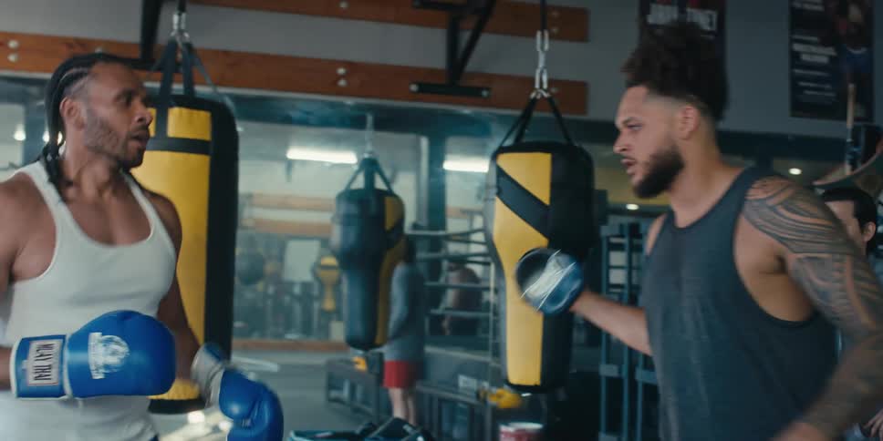 One man holds focus mitts for a boxer while their coach watches and end with a friendly hug in a gym