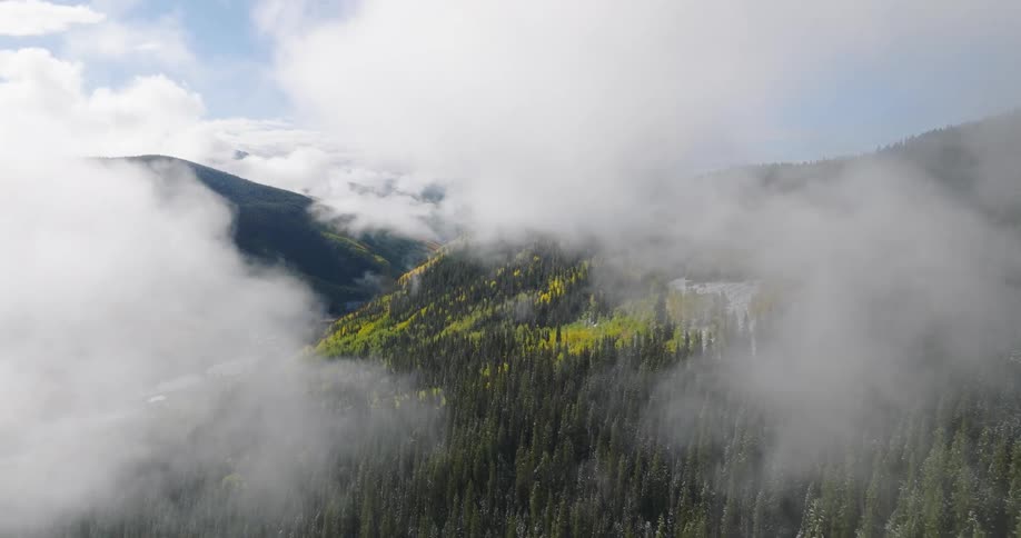 Aerial of clouds and a forested mountain range on an autumn day