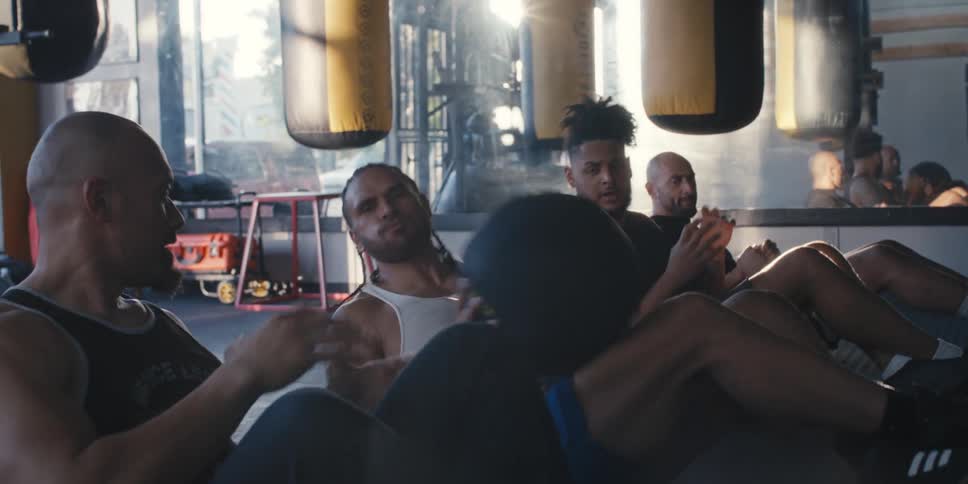 Four men pass a weighted ball while lying on the floor of a gym while the sun flares off a window