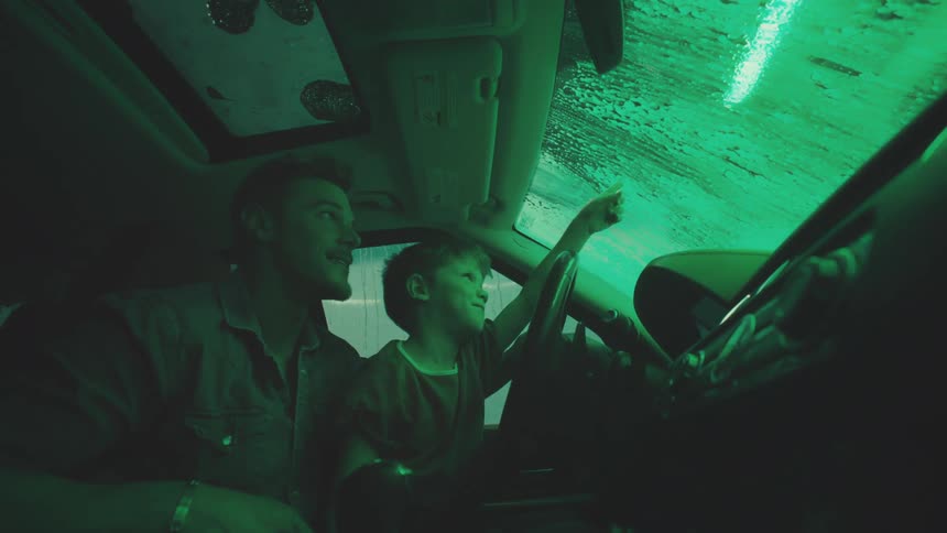 Father and son ride through a car wash while the son sits on his lap
