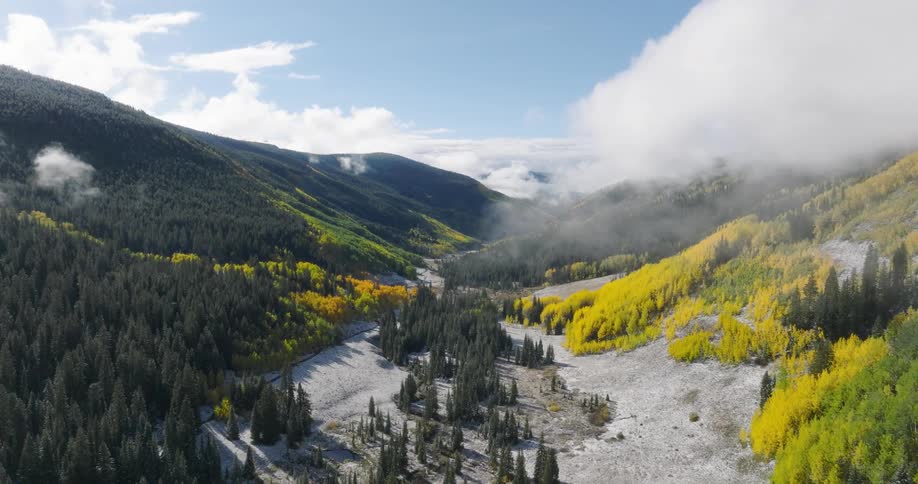 Patches of conifer and deciduous trees intermingle on the slopes of the mountains enclosing a valley in winter