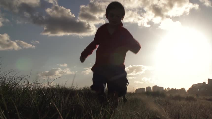 The children running and jumping in a field at sunset on a partly cloudy day