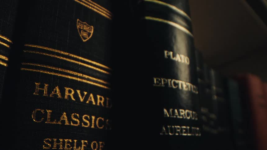 A row of books on a shelf with the spines bound in black leather and adorned with gold lettering that reads harvard classics and shelf of fiction
