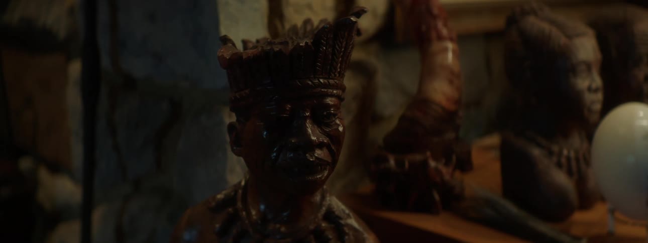 A wooden statue of a man wearing a headdress is displayed in a dimly lit room