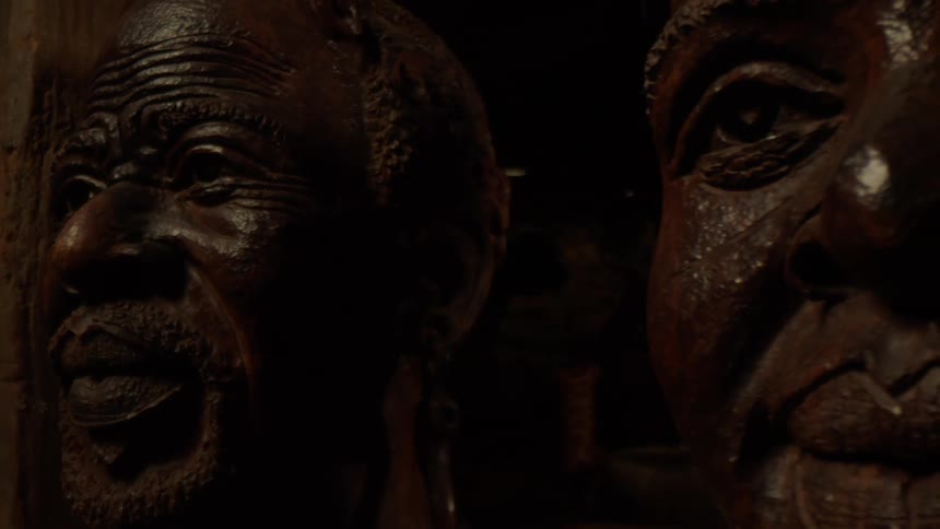 Two darktoned textured wooden sculptures of human faces with intricate carving emphasizing wrinkles and facial features evoking expressions of wisdom or contemplation