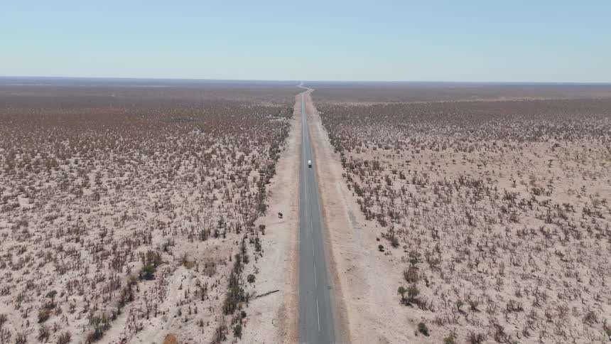 Straight road crosses a flat arid landscape with sparse vegetation