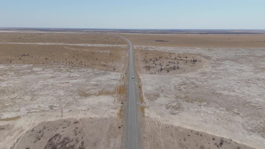 A truck drives on a remote highway through a large desert