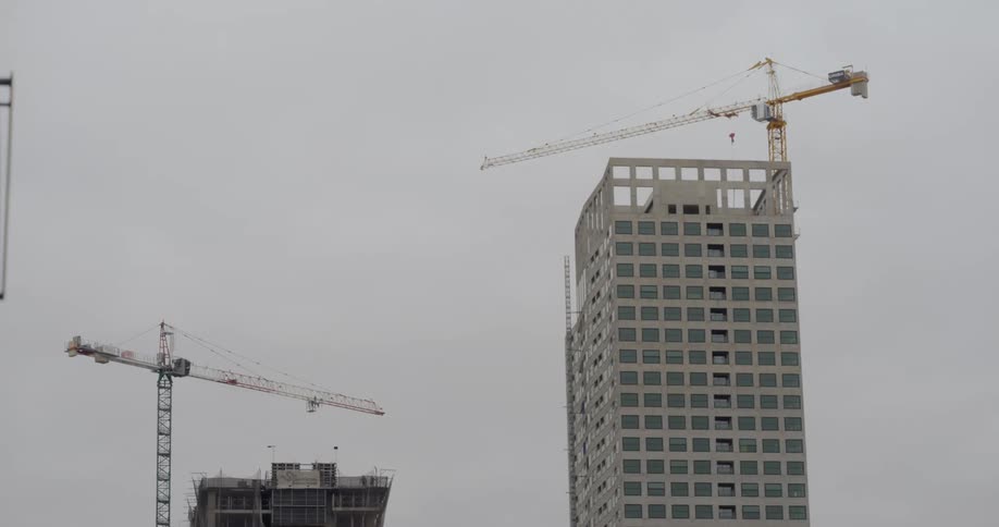 Construction cranes work on two high rises under construction on an overcast day