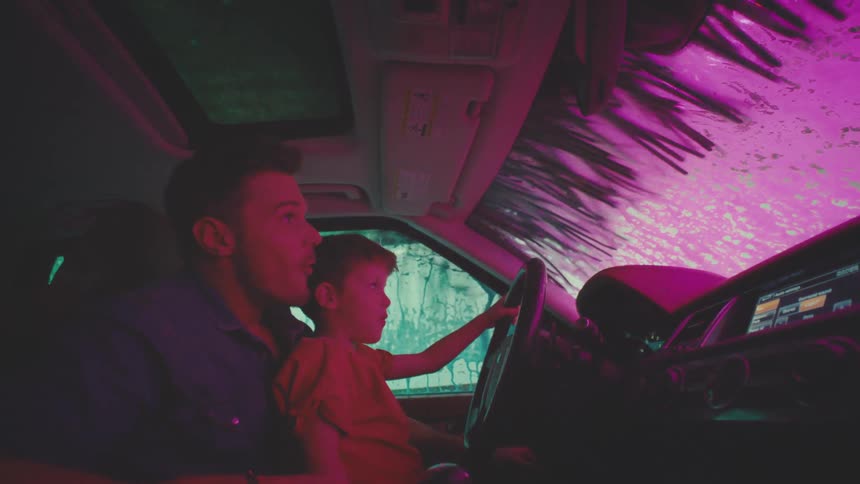 Father and son together inside the car having fun while a soap machine cleans the vehicle