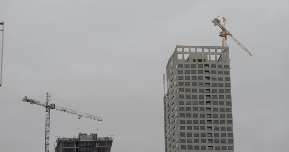 A crane spins around the top of a partially constructed high rise urban building
