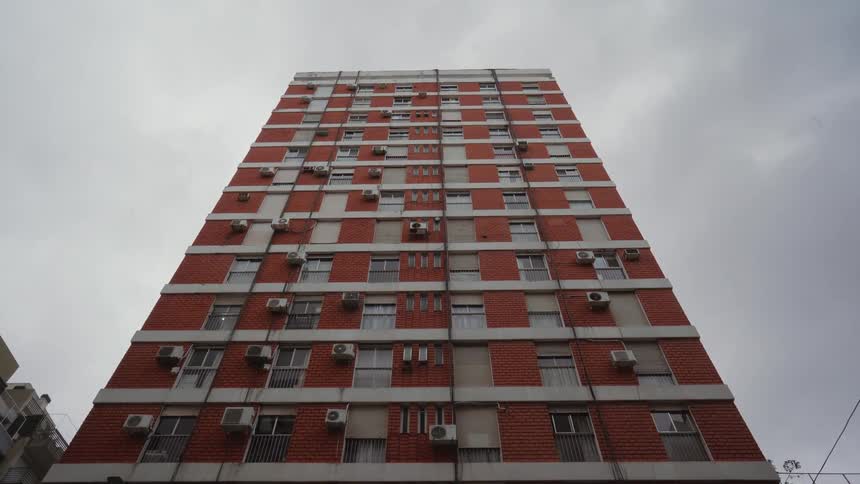 A large orange brick building with several windows and set against a cloudy sky
