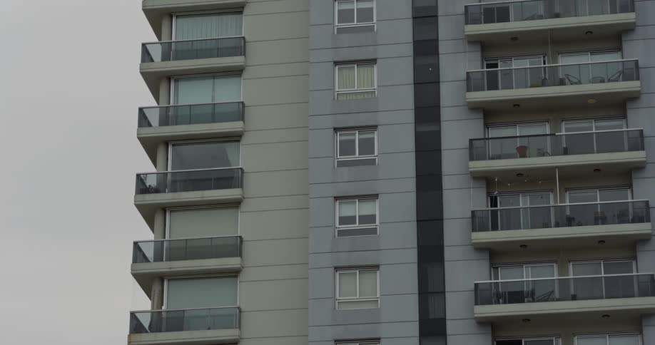 The facade of a large apartment building with several windows and balconies with glass parapets