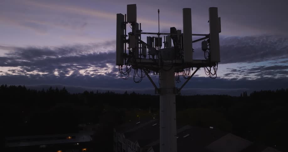 Subtle orbit and close approach toward the silhouette of a 5G network tower against an evening sky