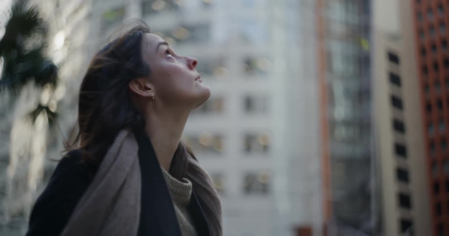 A woman gazing upwards her expression focused and reflective as she stands in a bustling urban environment