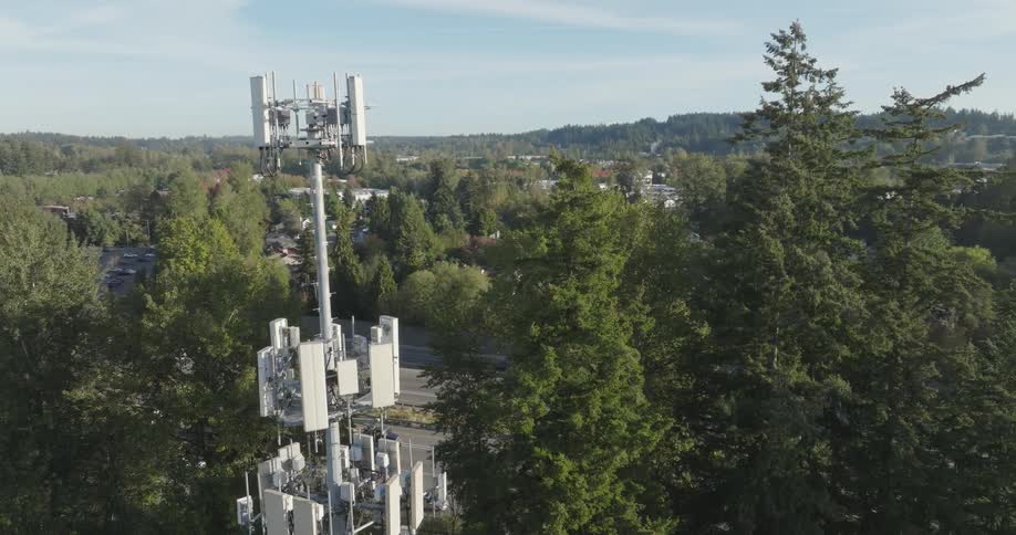 A multi network 5G tower works next to a large highway during the morning commute