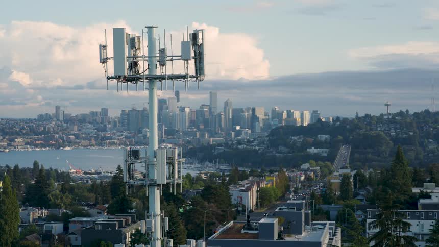 Clockwise orbit around a state of the art 5G cellular data tower working over a city neighborhood near downtown skyscrapers