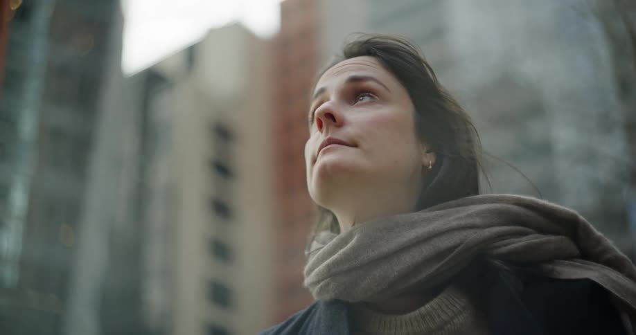 A woman in a scarf gazes upward in a city setting