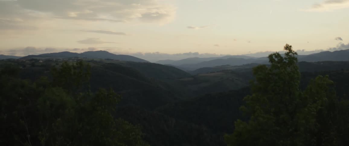 A view of a valley with distant forested mountains under a soft pale sky
