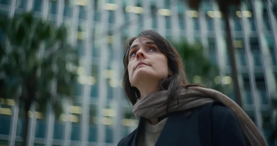 Black haired woman with brown scarf looking up with buildings around