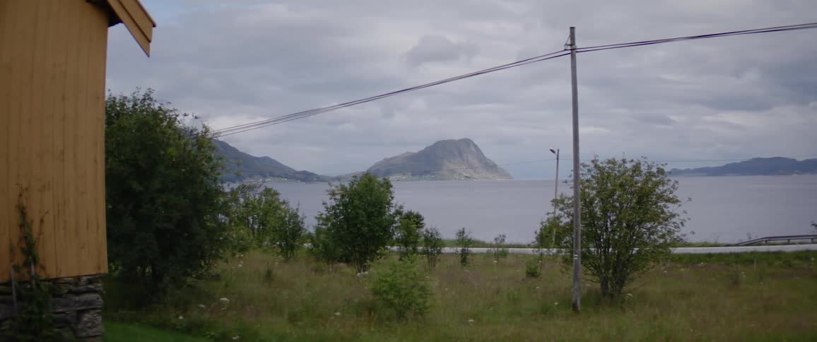 A scenic view from a wooden cabin featuring a grassy field a winding road a calm lake and a distant mountain