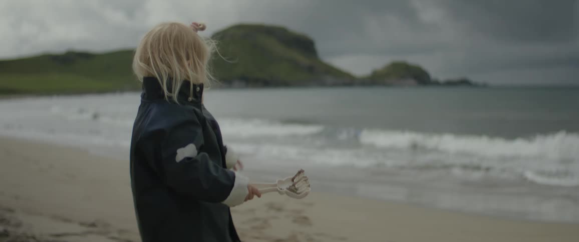 A young white girl holding a fake hand points at the tide coming in on a beach