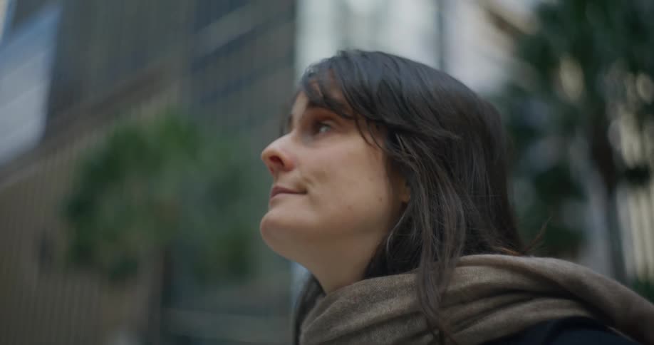A young woman stands in the middle of a city and stares at the large buildings