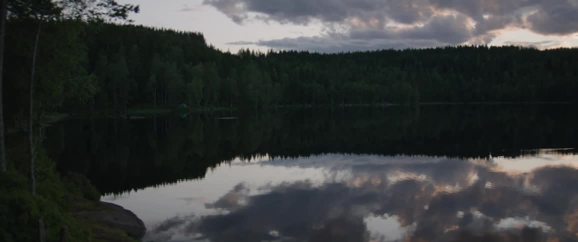 Scene of a lake reflecting the sky with clouds and the silhouette of trees on the shore