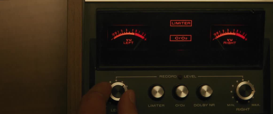 Closeup of a vintage audio recording device with vu meters and control knobs with a hand setting it