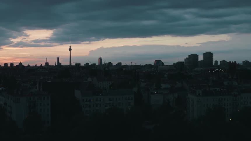Aerial view of a cityscape at dusk with a prominent television tower under a sky with dark clouds