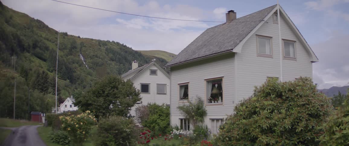 A large white wooden house in a rural area with lots of vegetation around it