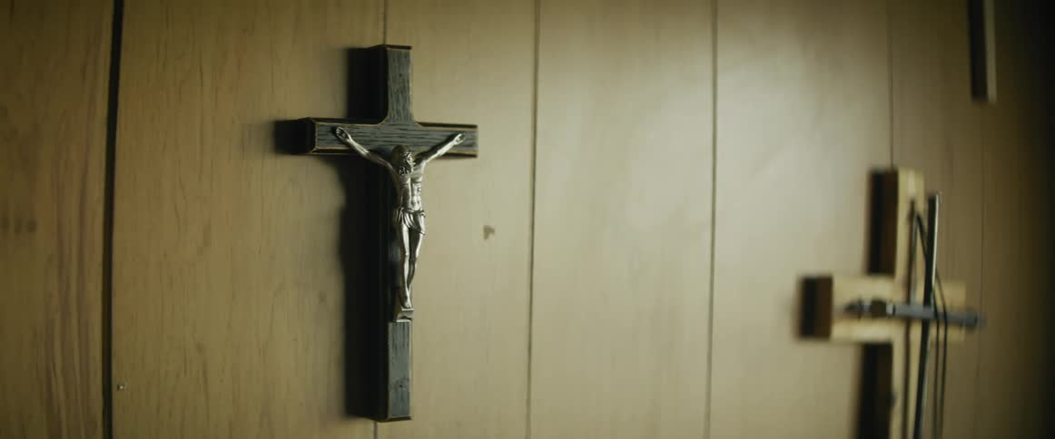 A cross with an image of jesus hanging on a wooden wall and on the right side there is a larger cross