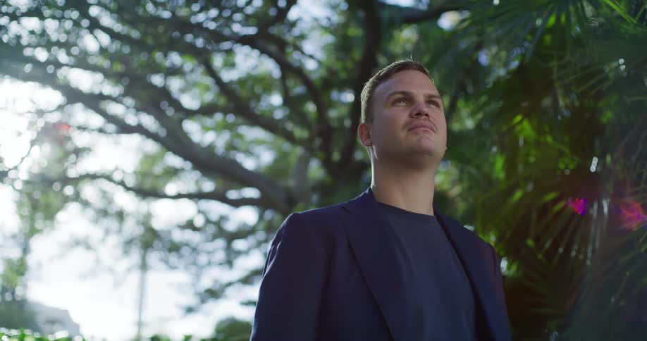 Man in tshirt and blazer next to trees