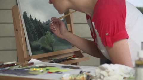 A short-haired woman painting a landscape on canvas