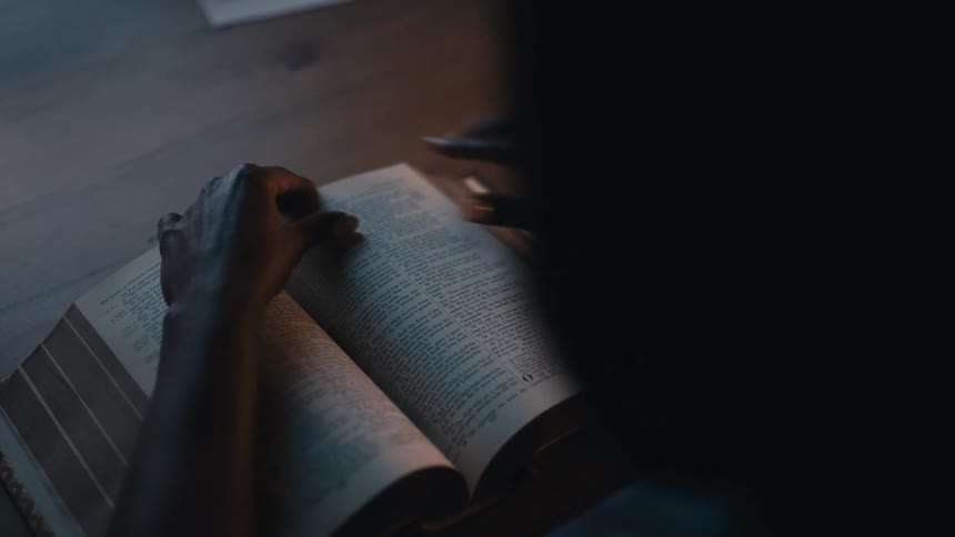 Woman sitting at table and picking up a bible and opening it