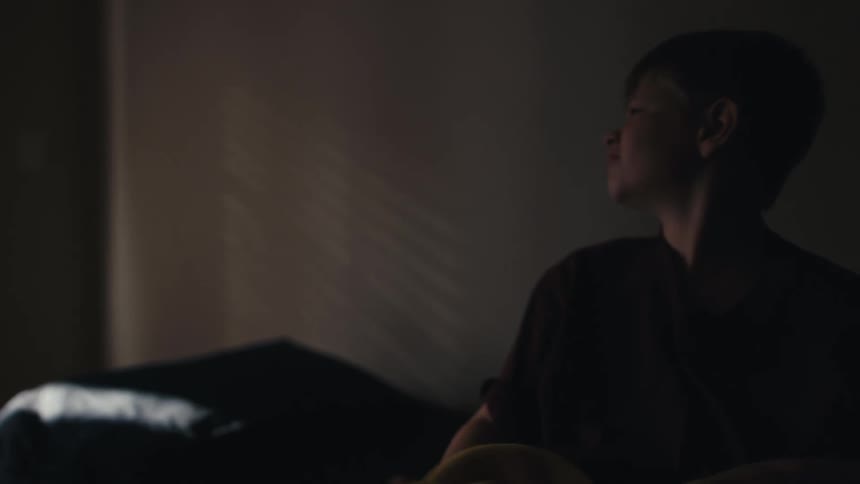 A young boy wakes up in bed and puts on his tennis shoes