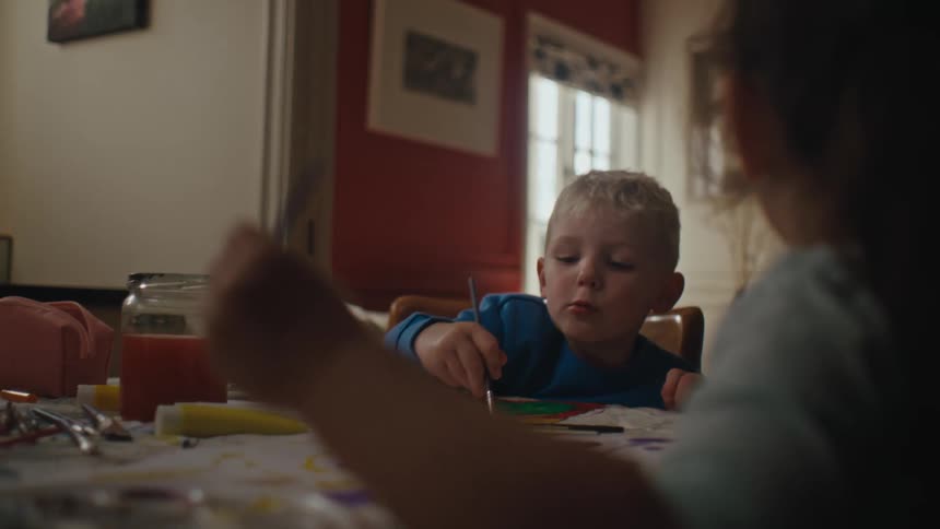 A couple of children paint and draw with watercolors on paper at a table at home