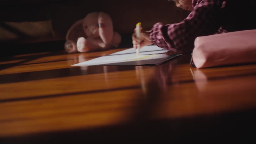 A female toddler scribbles frenetically on a whiteboard on a dining room table