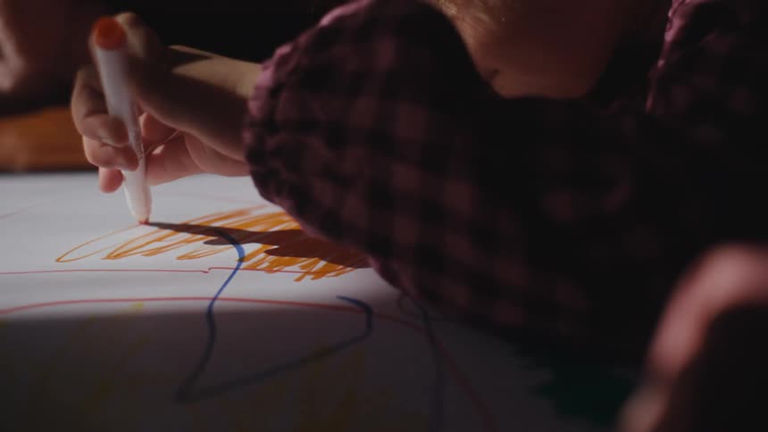 A young girl scribbles orange lines on a whiteboard
