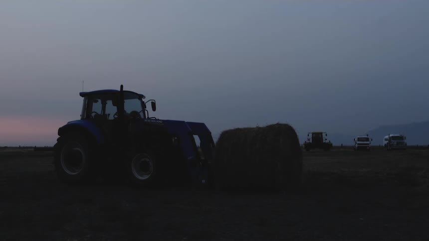 Agricultural grass roll next to a tractor and other machinery in the background in a field