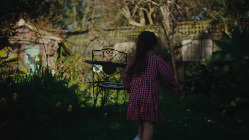 A woman with a ponytail wearing a red dress runs playfully in the backyard