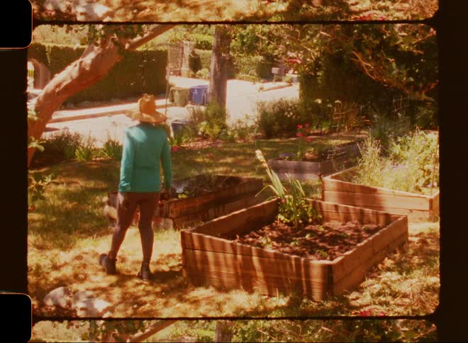 Woman with a hat walking in the backyard with vegetable garden