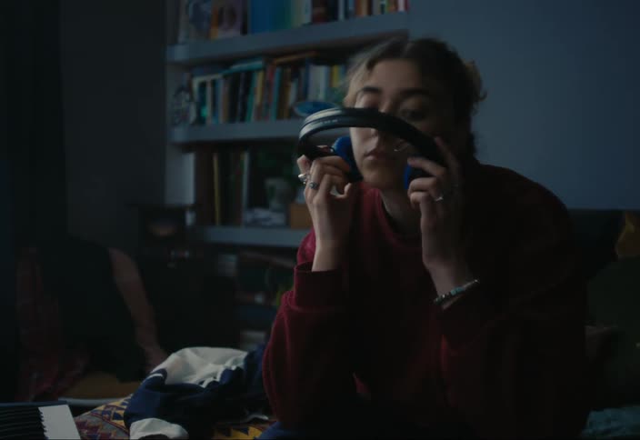 Teenage girl sitting on bed with music mixer and taking off her headphones