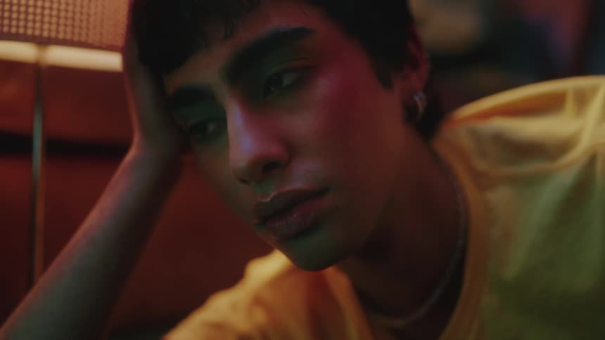 Closeup of a man with makeup dozing off in front of blinking lights in a dimly lit room